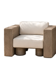 A modern outdoor armchair with a thick white cushioned seat and backrest, set in a minimalist patio environment with a stucco wall and a large planter in the background.
